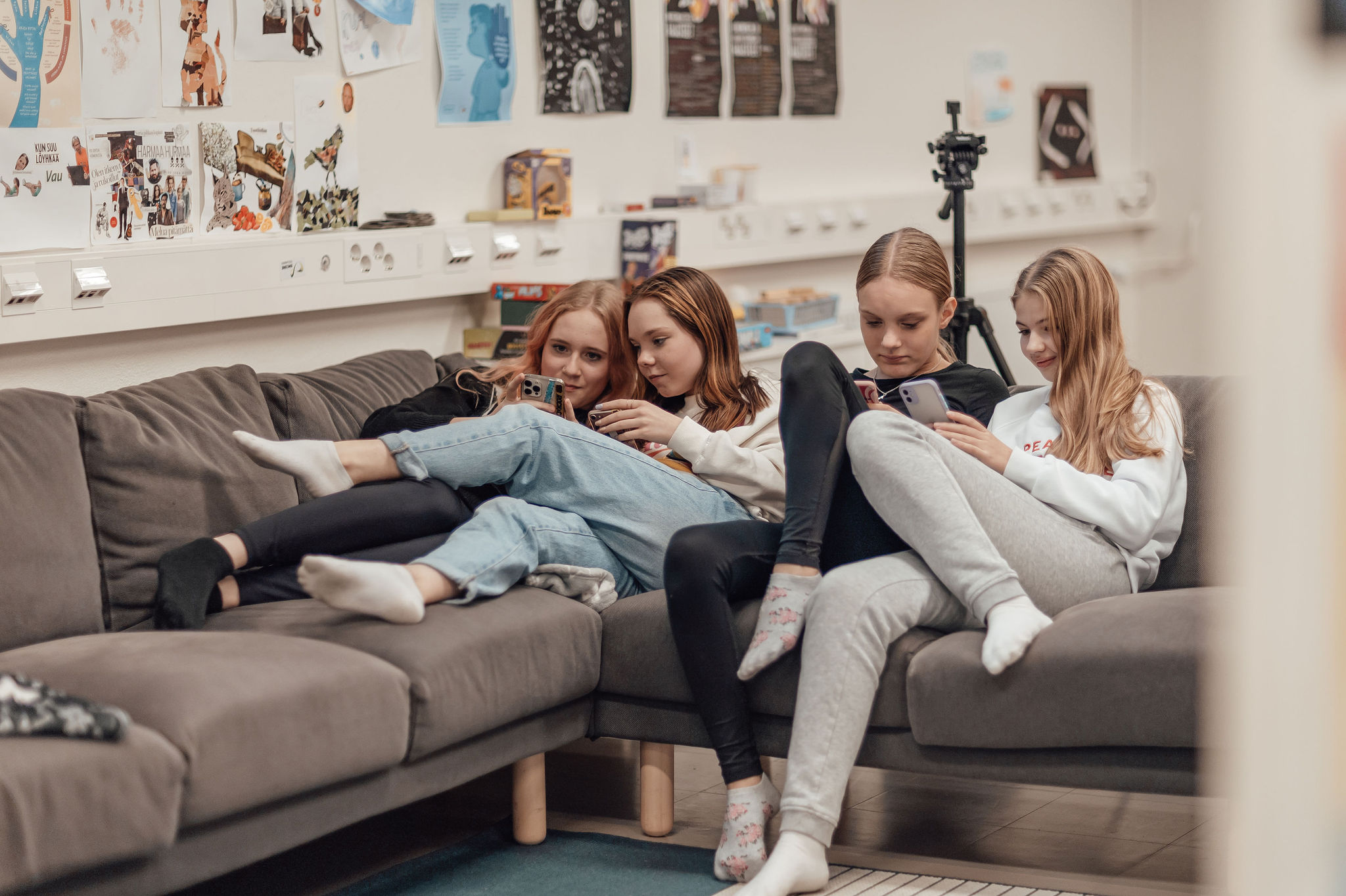 Neljä tyttöä istuu sohvalla ja katsoo puhelimia