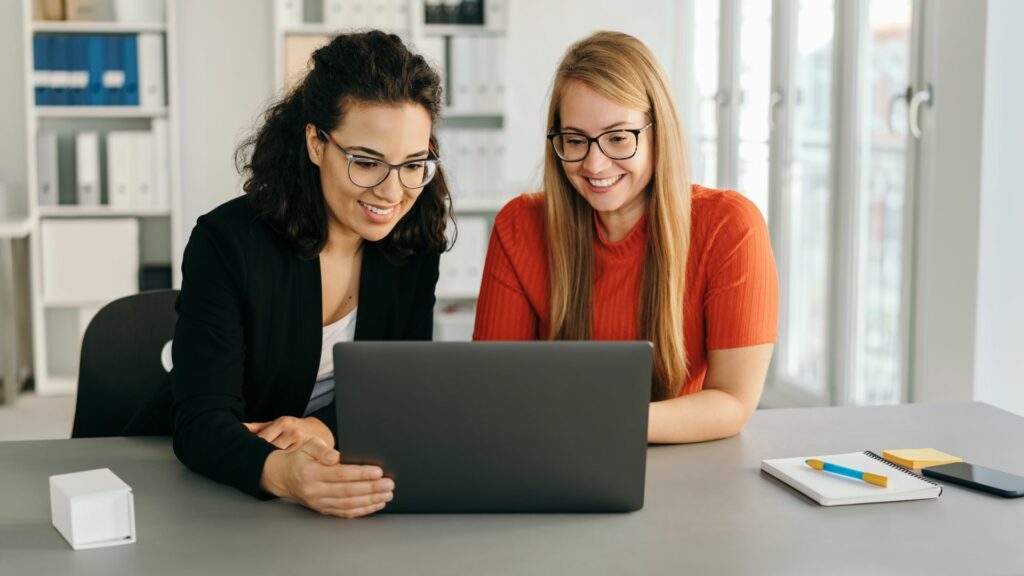 Kaksi naista katsoo toimistossa edessään olevan kannettavan tietokoneen näyttöä.