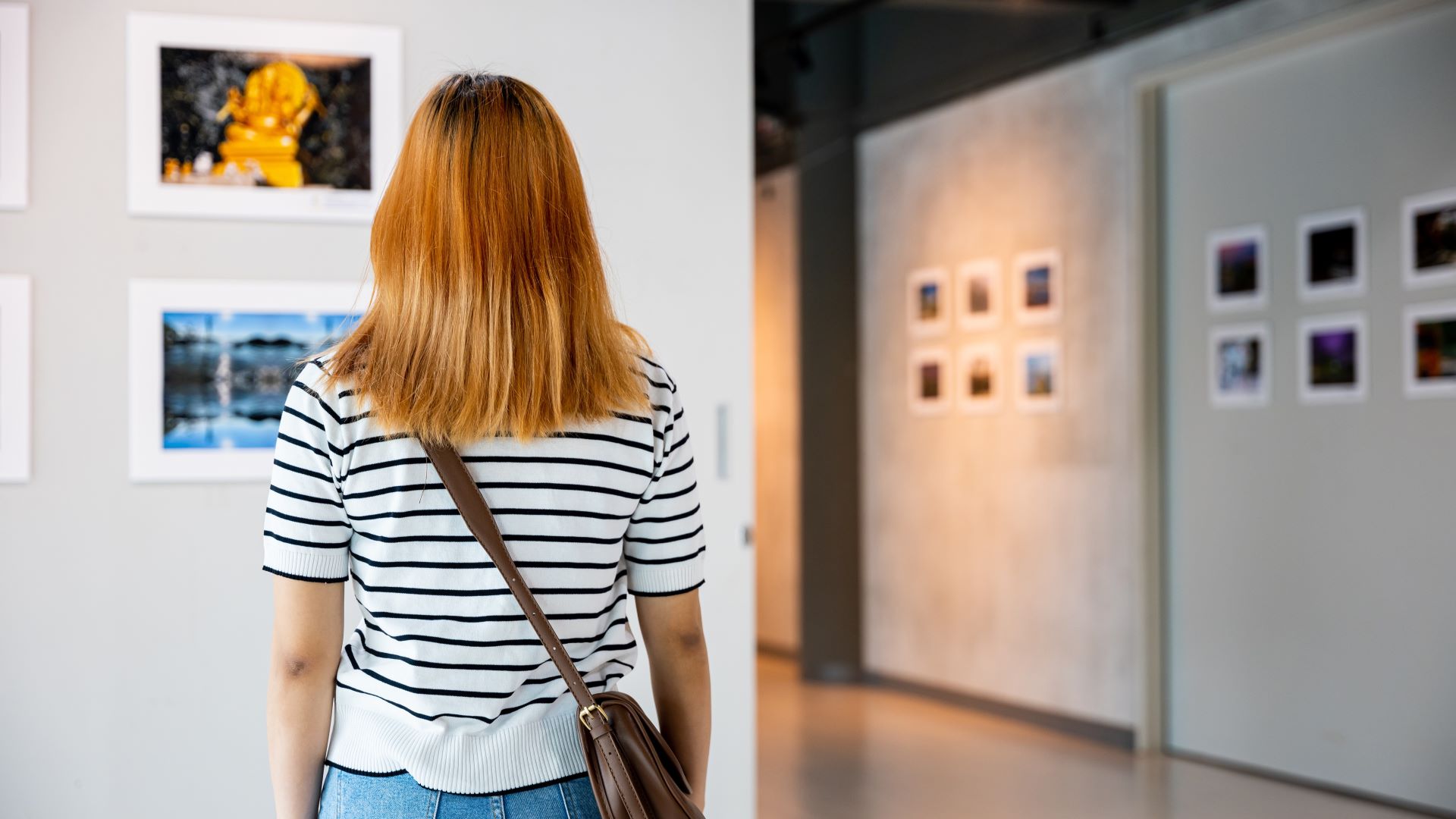 Nainen seisoo selin kameraan ja katsoo seinälle ripustettua taulua.