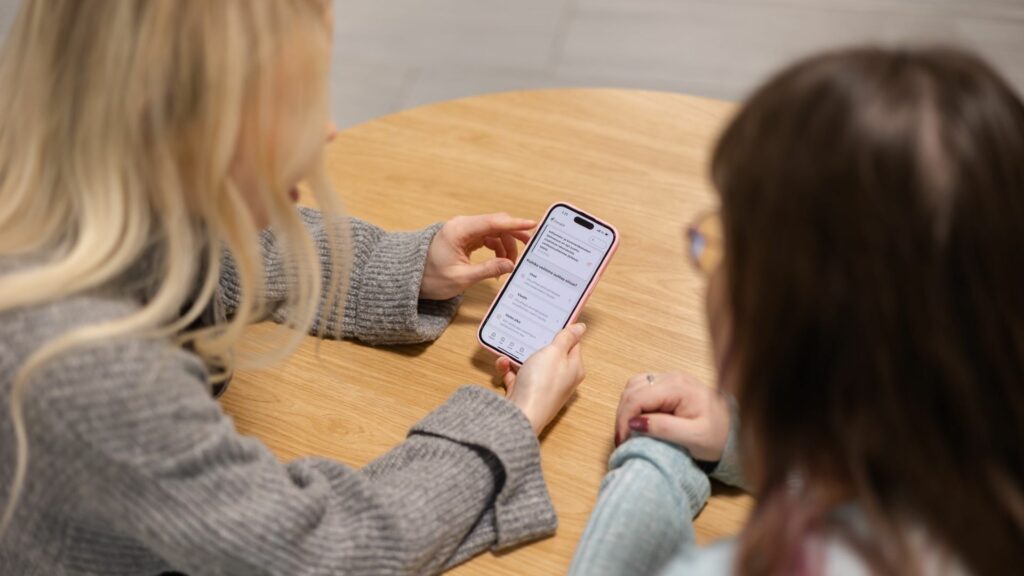 Kaksi naista katsoo pöydän ääressä älypuhelimen näyttöä. Näytöllä näkyy OmaEP digipalvelu.