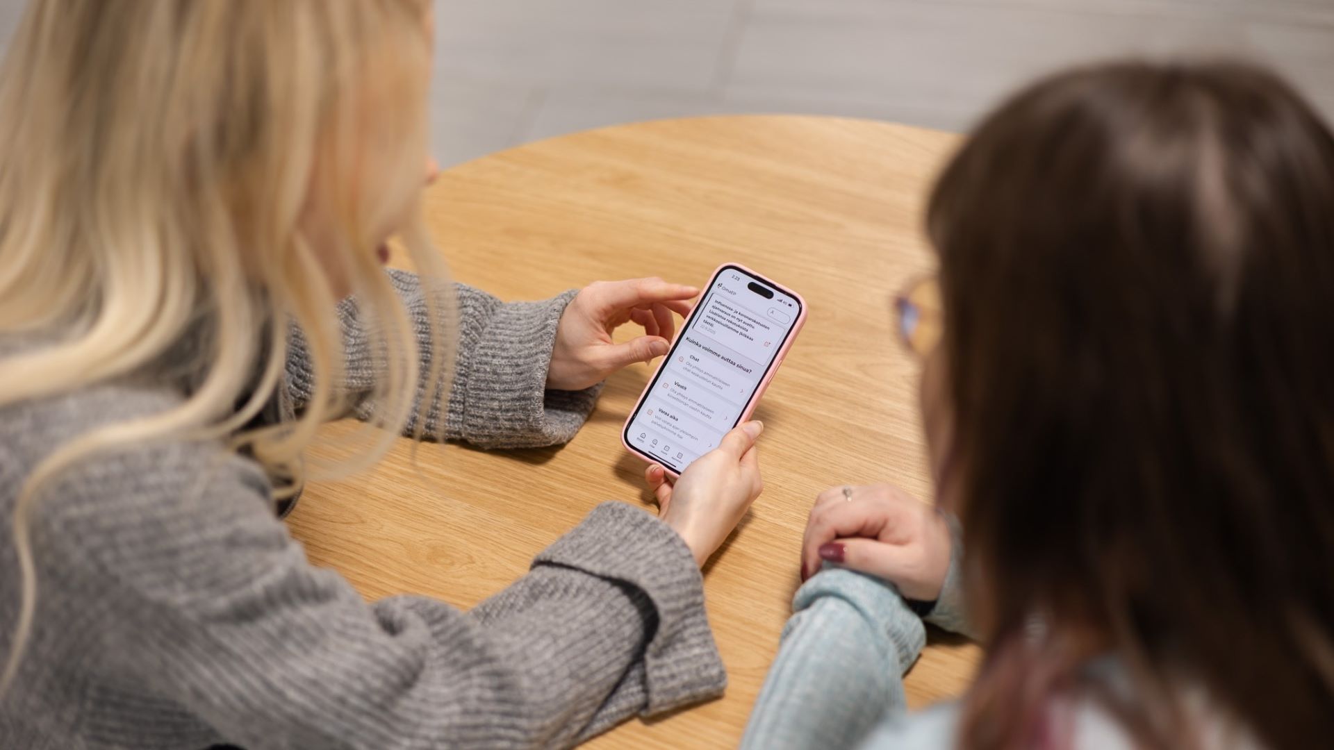 Kaksi naista katsoo pöydän ääressä älypuhelimen näyttöä. Näytöllä näkyy OmaEP digipalvelu.