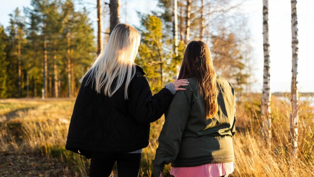 Kaksi naista seisoo järven rannalla selät kameraan päin.