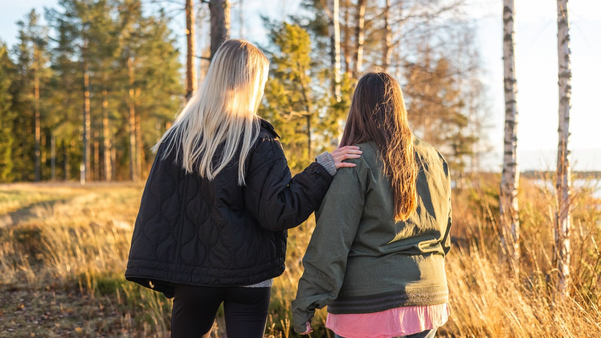 Kaksi naista seisoo vierekkäin selkä katsojaan päin. Toinen nainen pitää kättä toisen naisen olkapään päällä.